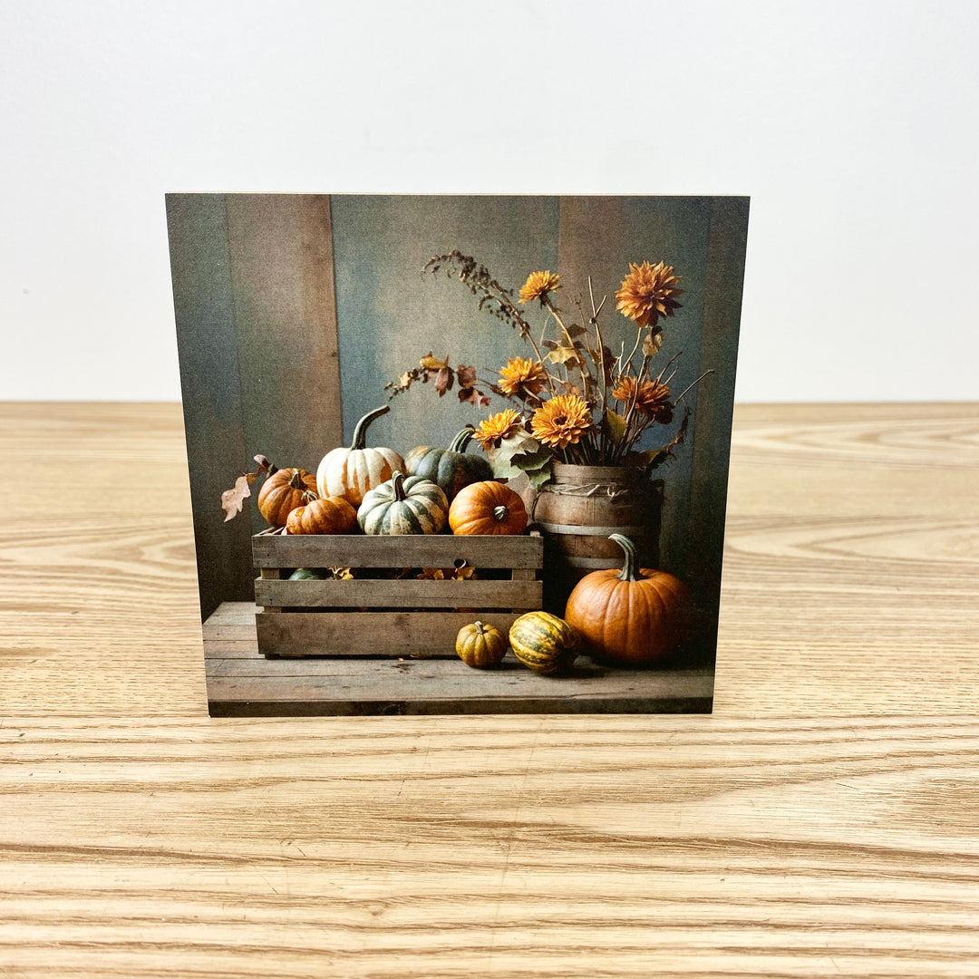 Still life arrangement with pumpkins, gourds, and flowers on a wooden surface.