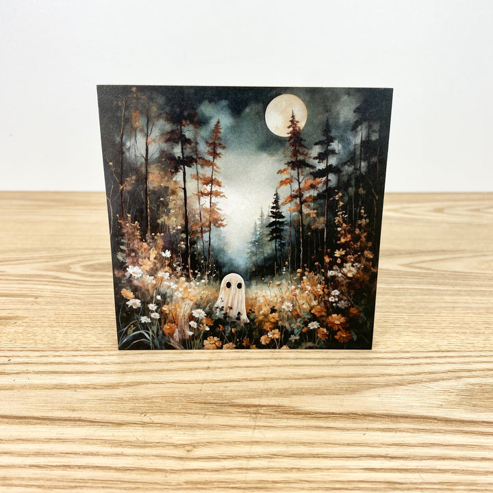 Greeting card with a ghost in a forest design on a wooden surface