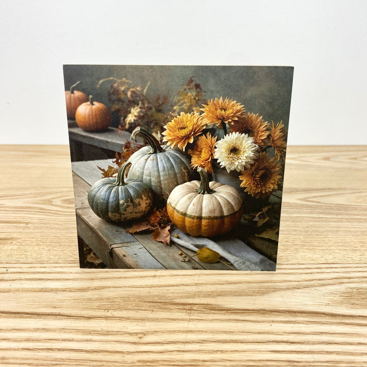 Autumn-themed card with pumpkins and flowers on a wooden surface