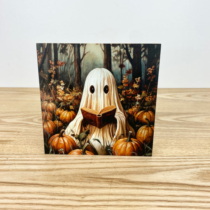 Block with a ghost reading a book surrounded by pumpkins in a forest setting
