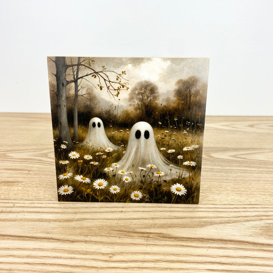 Two ghostly figures standing in a field of flowers with a forest background on a wooden surface.