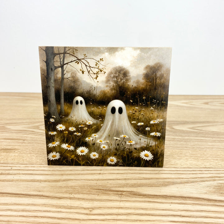 Two ghostly figures standing in a field of flowers with a forest background on a wooden surface.
