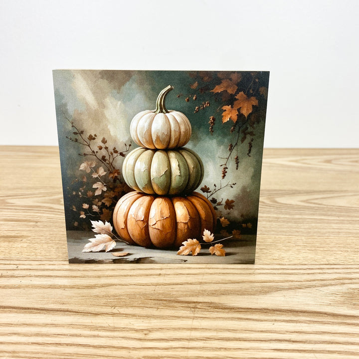 Stack of pumpkins with autumn leaves on a wooden surface