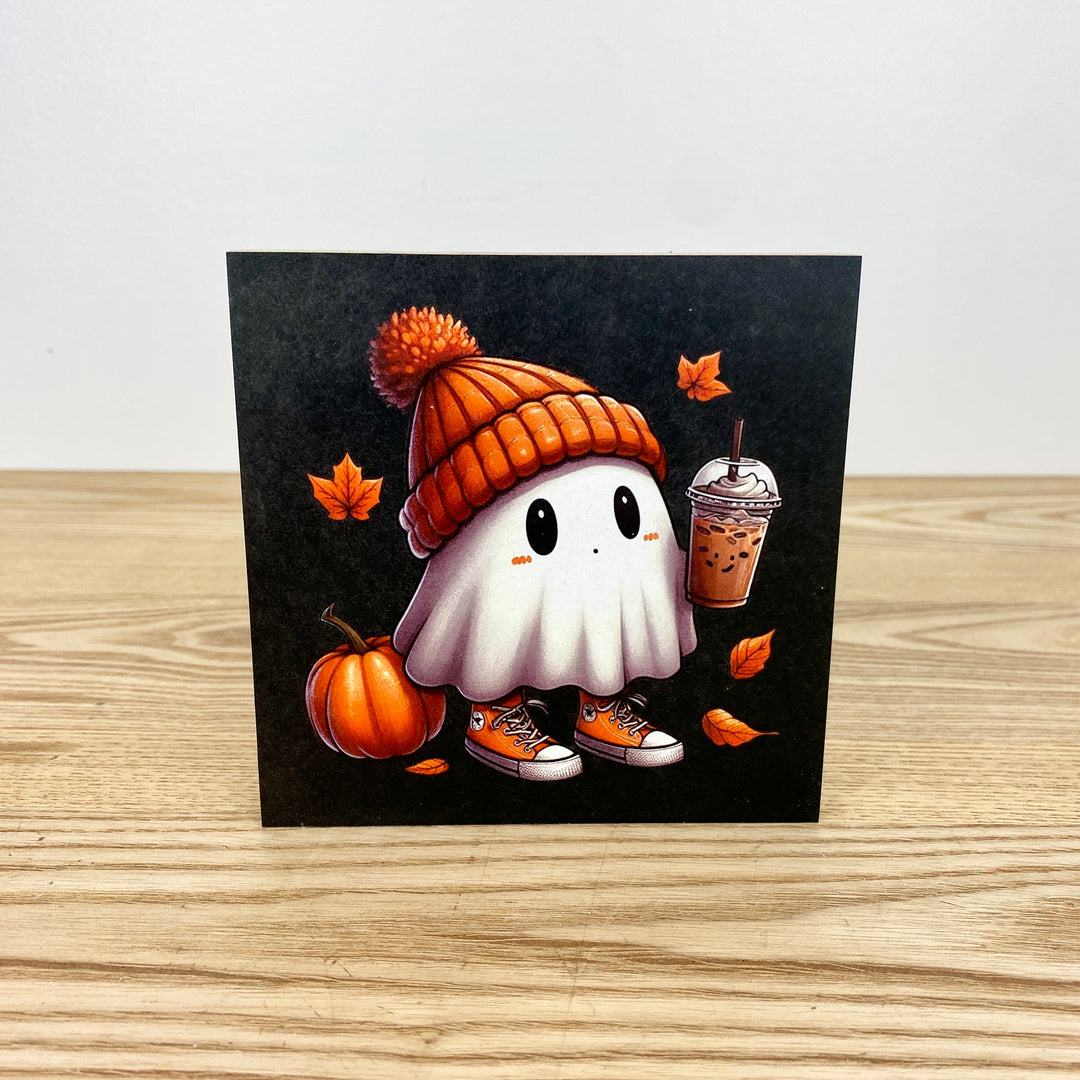 Cartoon ghost in an orange beanie with a pumpkin, coffee cup, and autumn leaves on a black background.